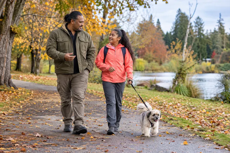 A girl and her father walk their dog together along a park path.