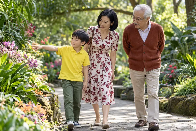 Three generations pause together while a child notices a flower in a garden.